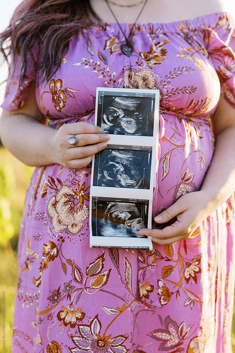 close up of woman in pink maternity dress holding ultrasound picture