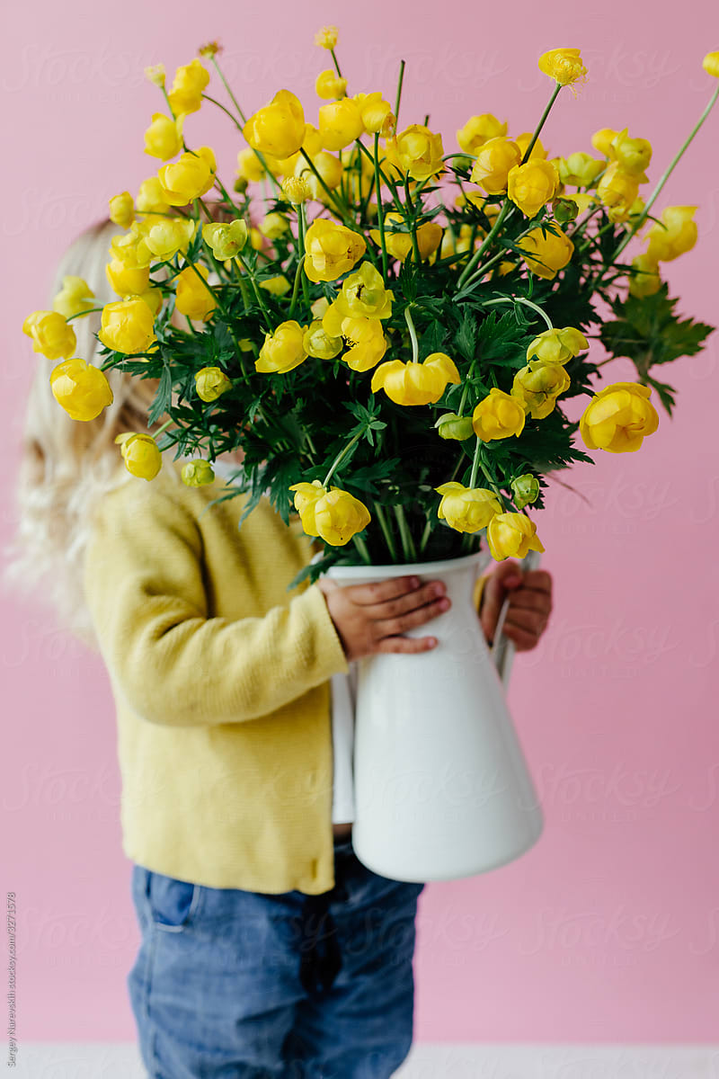 Faceless child with jug of yellow buttercups on pink background