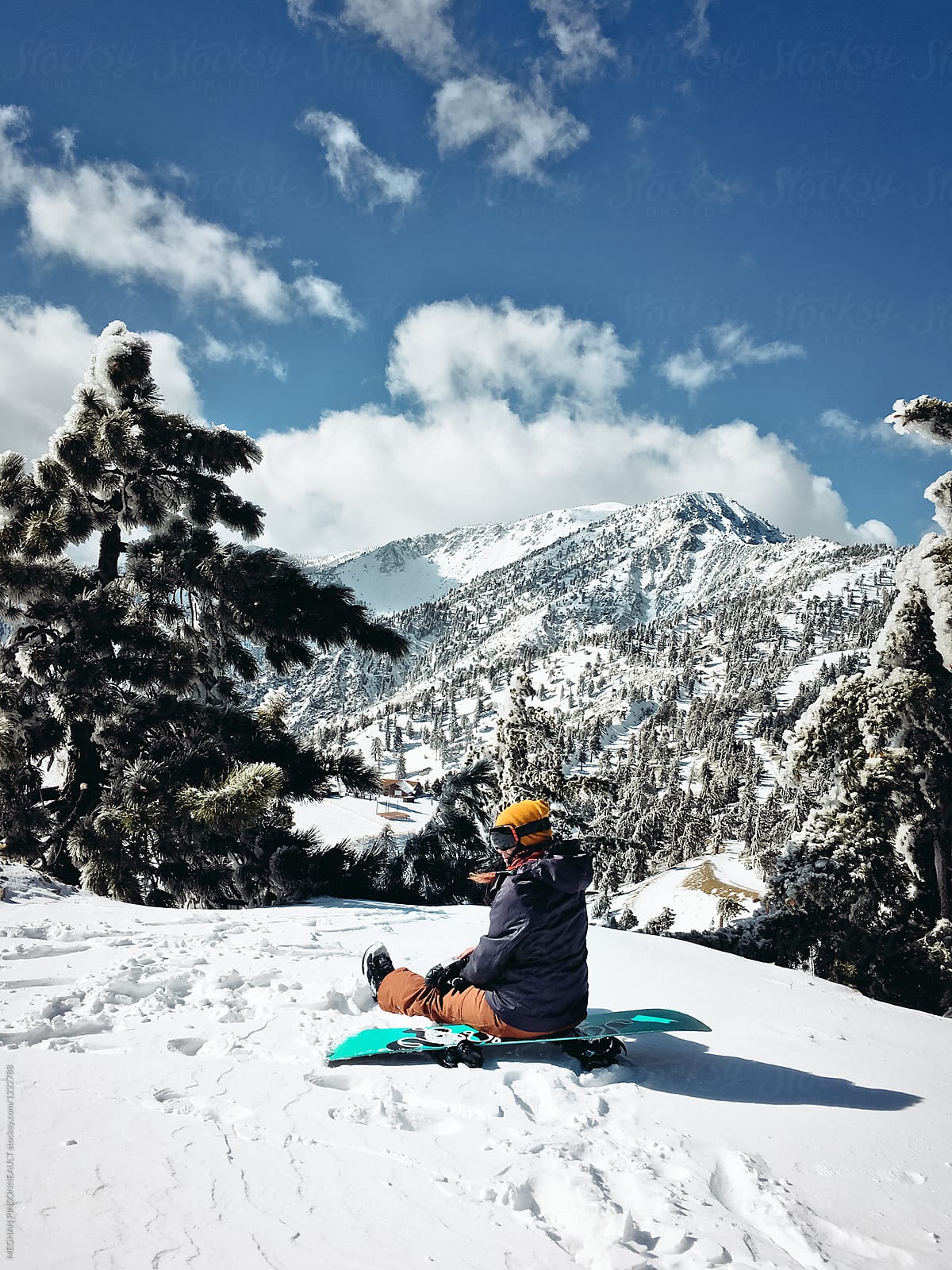 Female Snowboarder Resting on Board with Beautiful Snowy Mountains