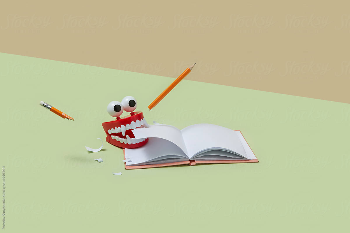 Red plastic jaws biting pencil and blank book.