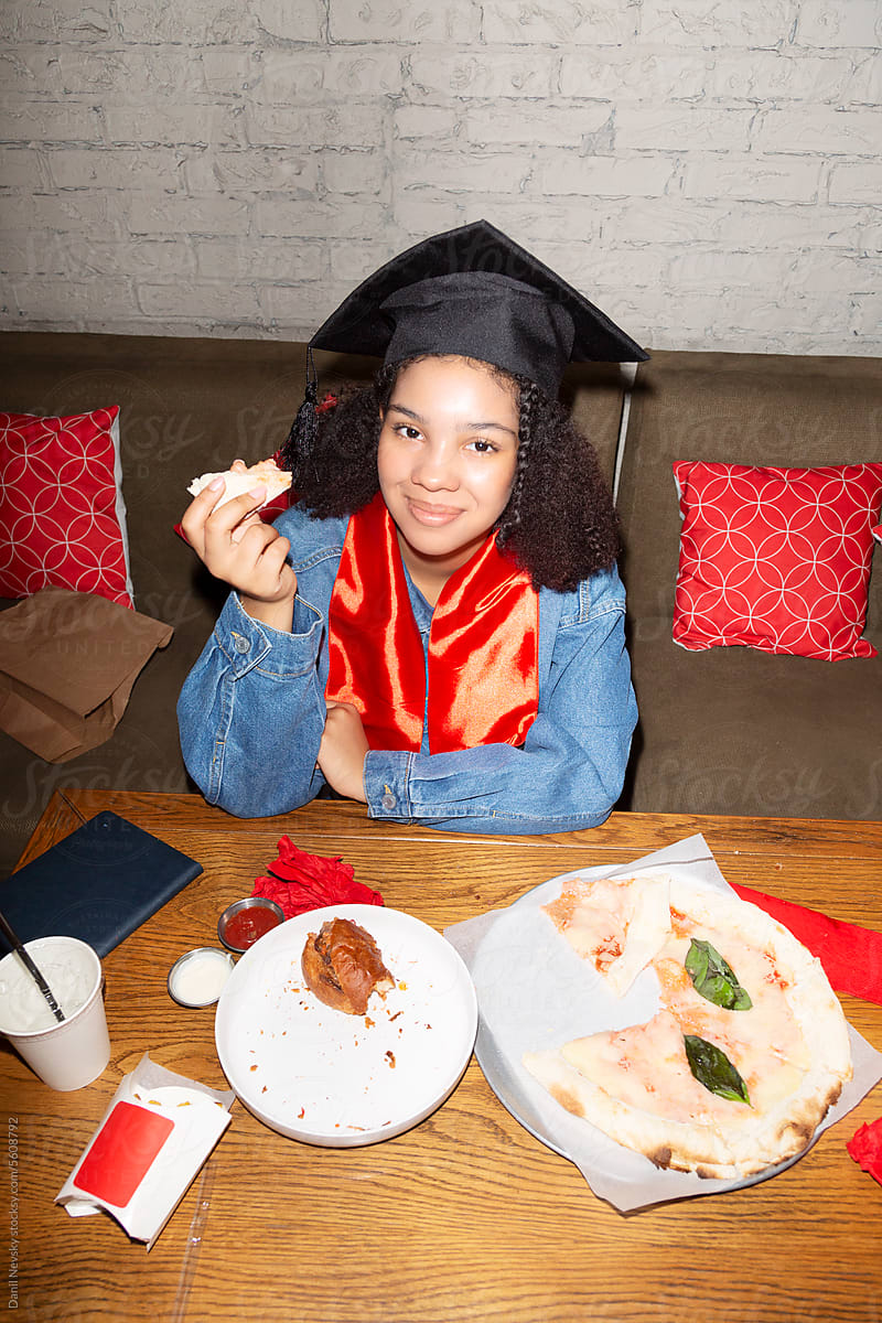 Smiling black girl eating pizza after graduation