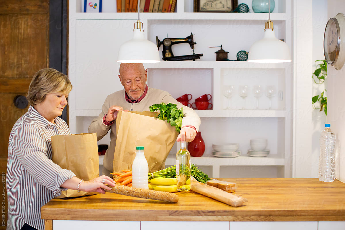 Elderly couple unpacks healthy market food in their kitchen.