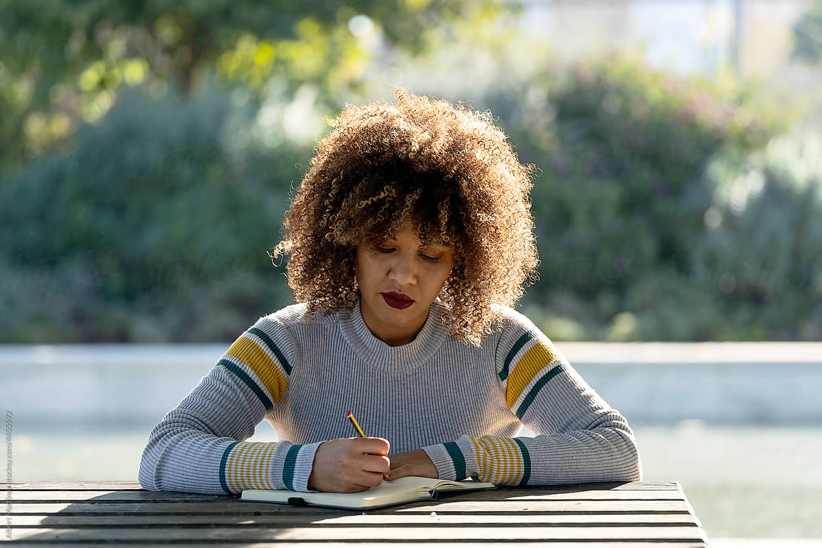 Curly haired woman taking notes in notebook in park