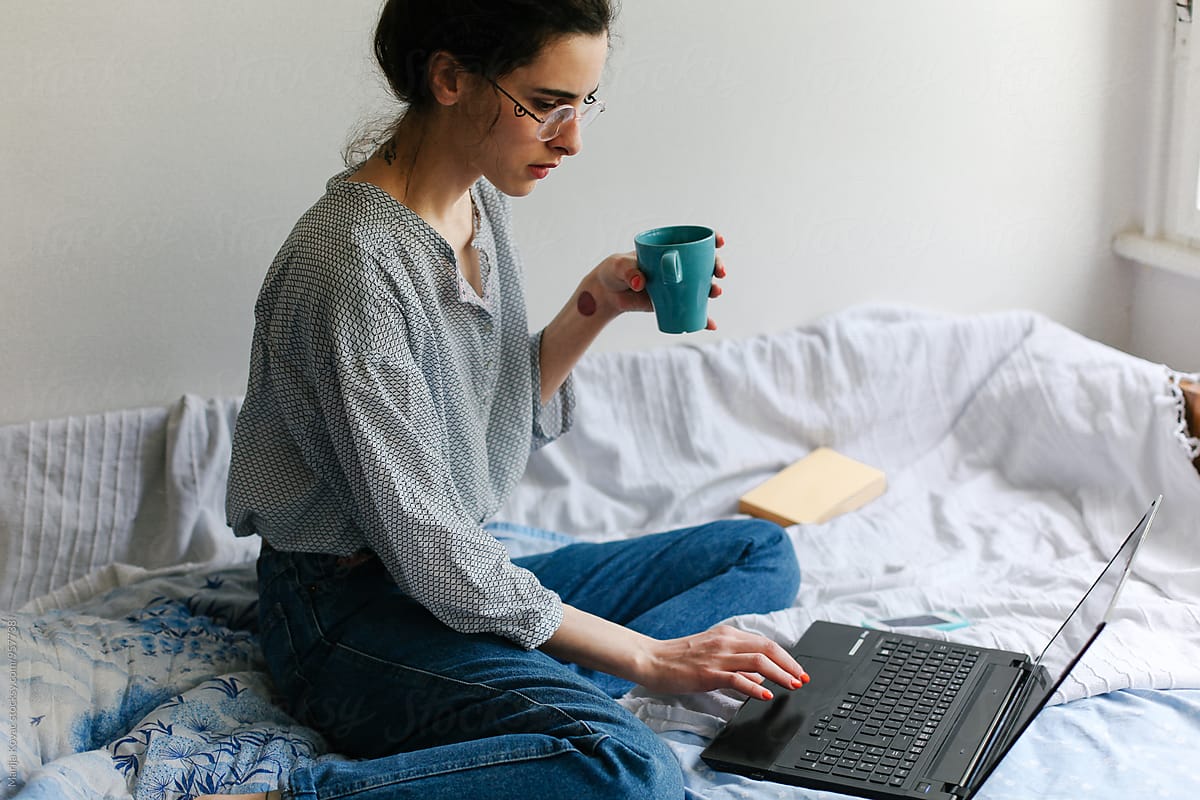 Woman Drinking Coffee On The Bed Using Her Laptop Del Colaborador De Stocksy Marija Kovac