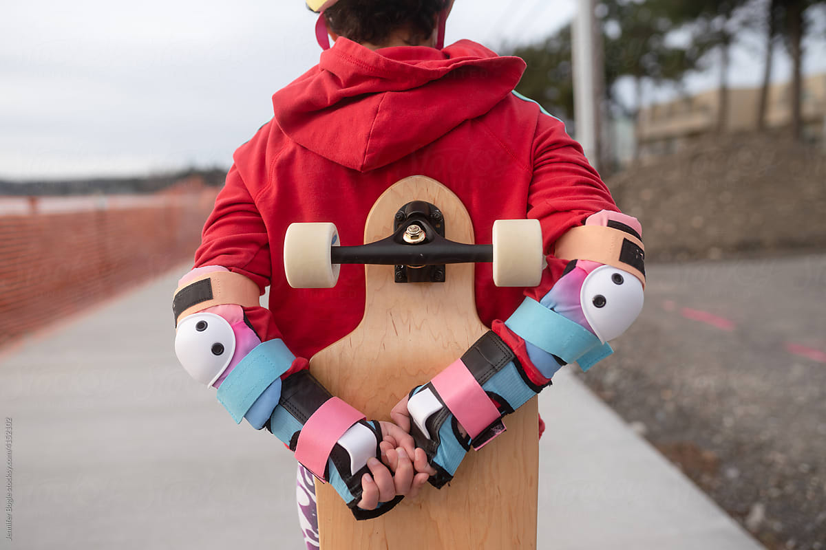 Girl in safety pads holds skateboard