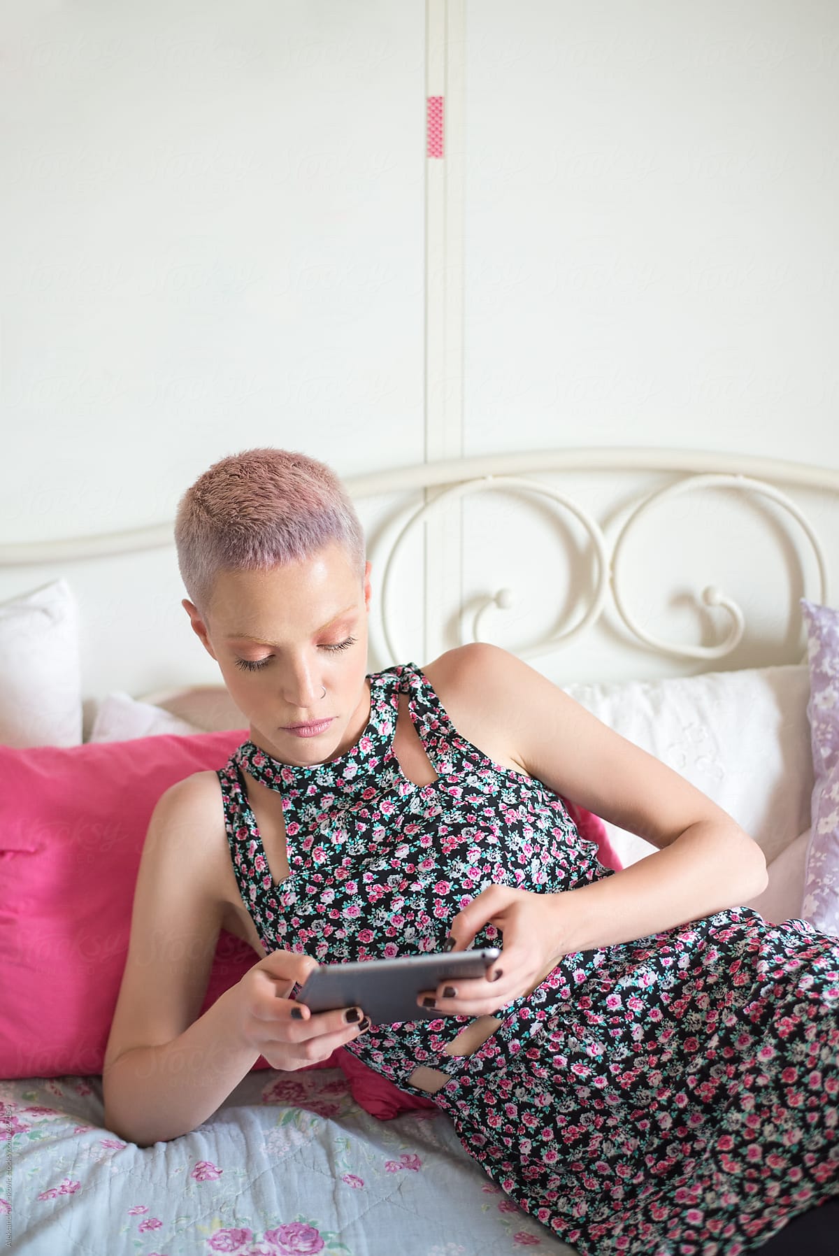Stylish Woman With Pastel Pink Hair Lying On The Bed And Using Tablet Computer