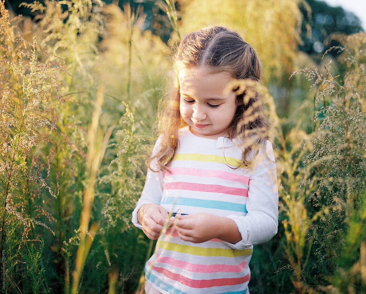 Portrait Of A Beautiful Young Girl Playing In A Field Of Tall Grass By Stocksy Contributor