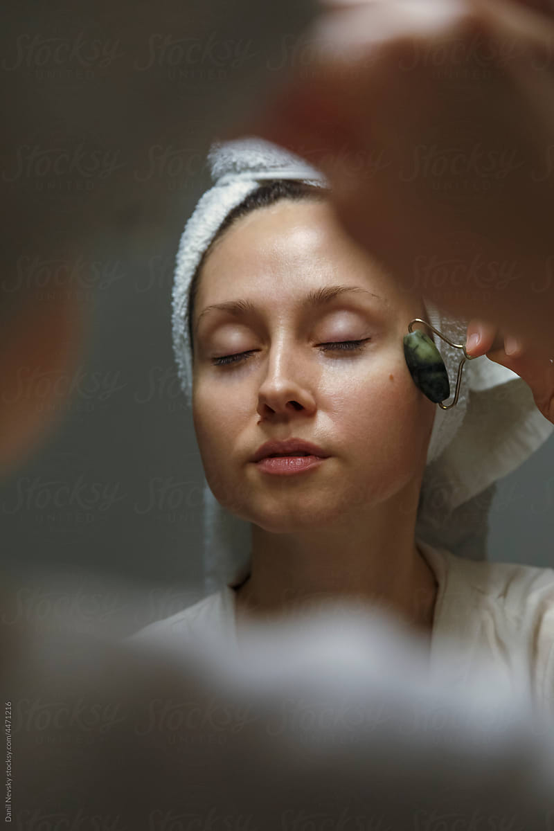 Lady massaging face with roller near mirror