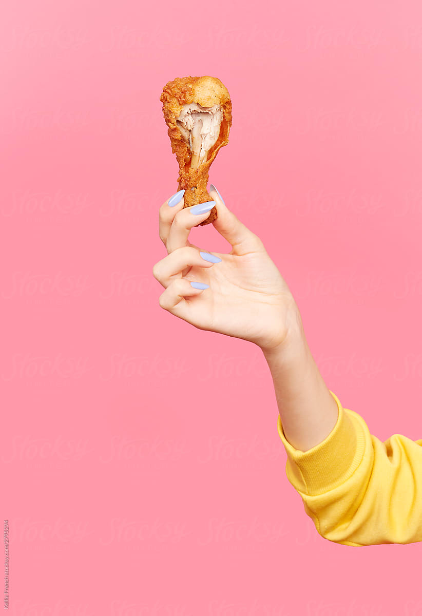 Woman holds bitten fried chicken drumstick in the air