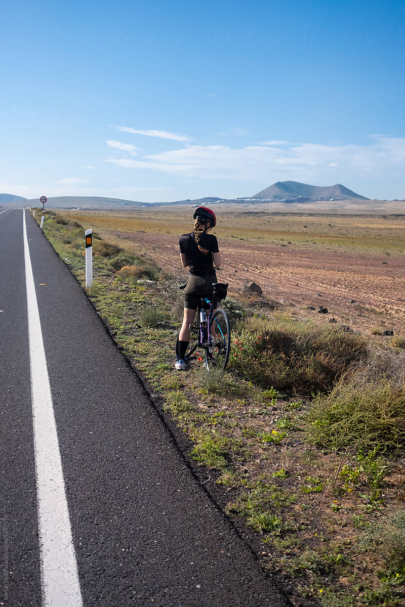 A female cyclist in sportswear, pausing beside the road