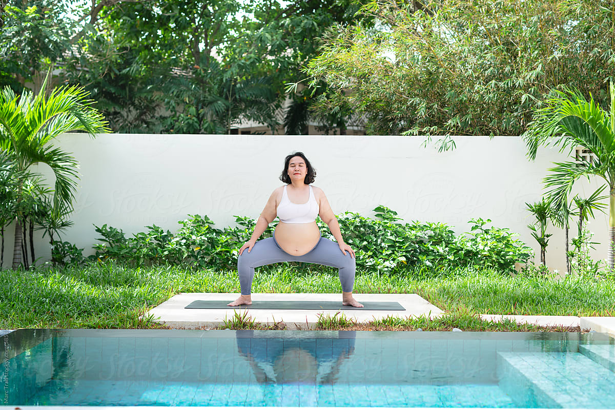 Pregnant woman doing yoga beside the pool.