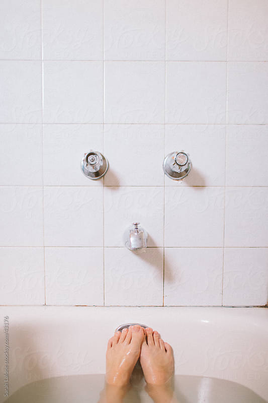 A woman\'s feet in a bathtub with tile and faucet.