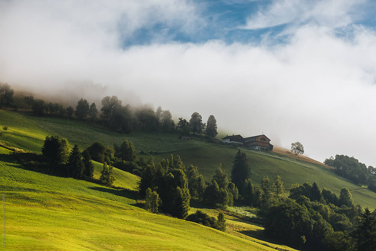 Green hill with trees and houses covered in fog and clouds