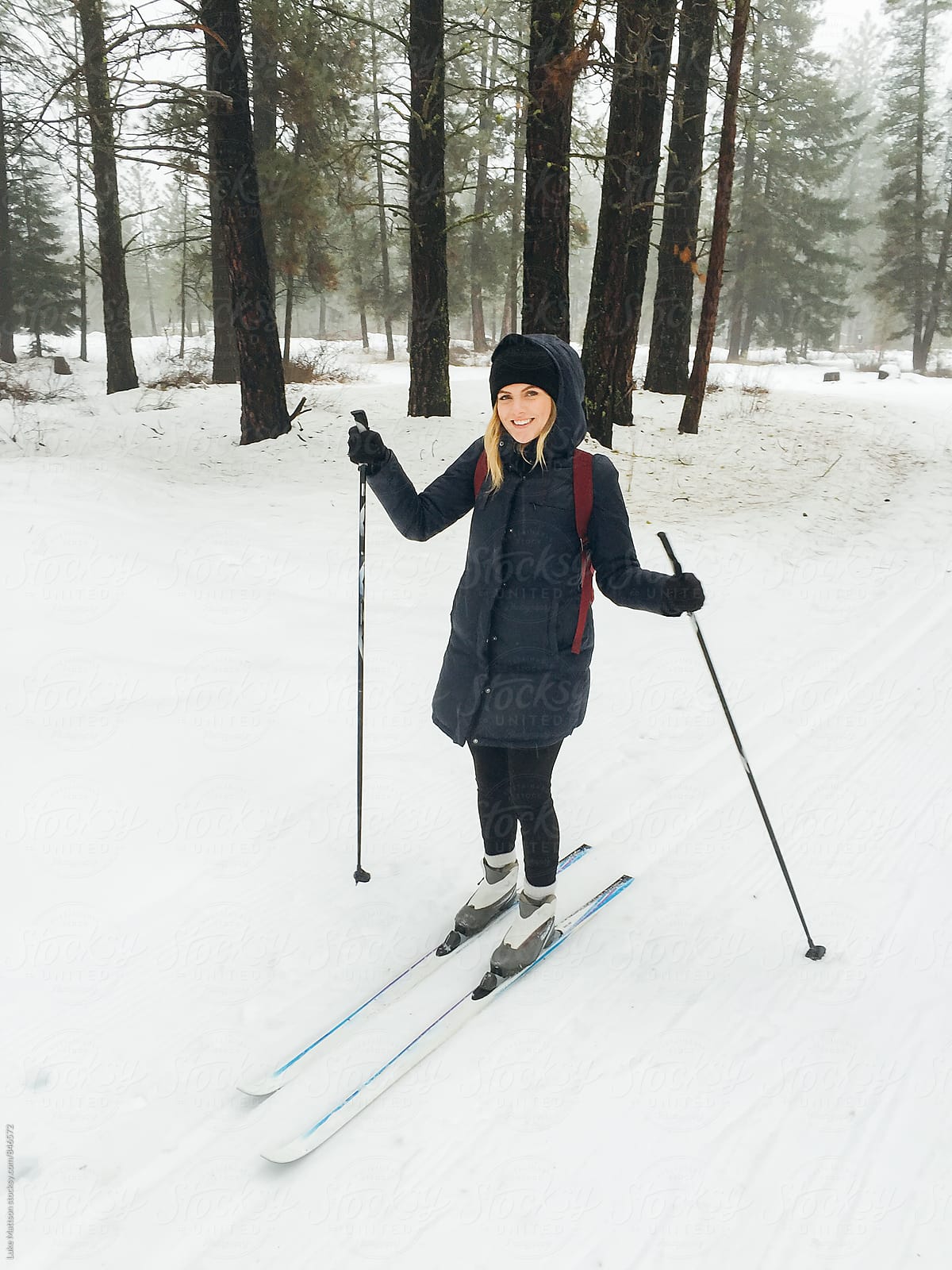 Smiling Young Blonde Woman Cross Country Skiing Along Snowy Trail Through Winter Forest