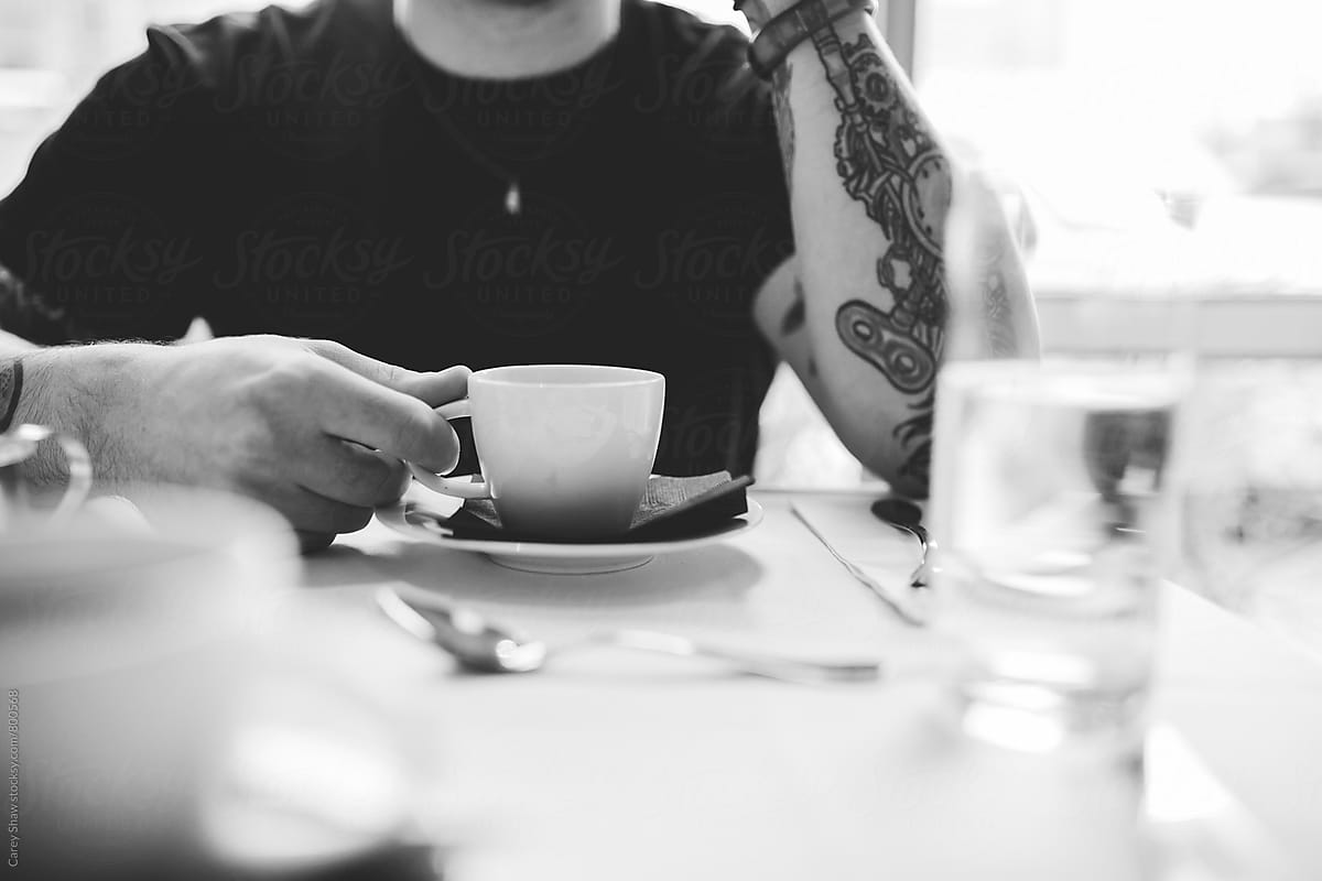Black and white portrait of young man with tattoos drinking coffee