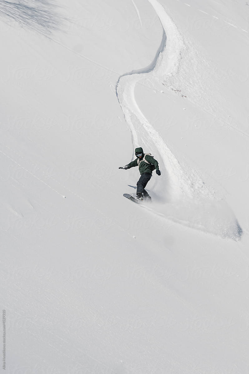 Active man riding snowboard down snowy mountain slope