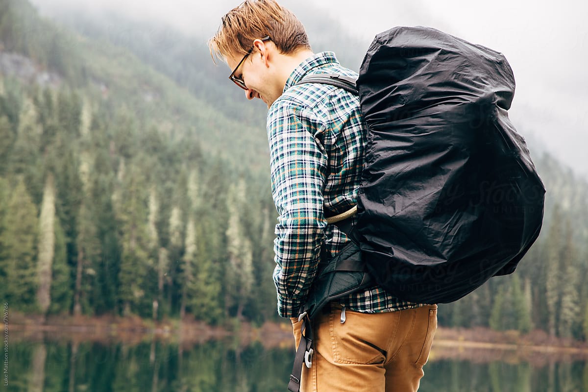 Young Man Wearing Backpack Standing By Subalpine Forest Lake
