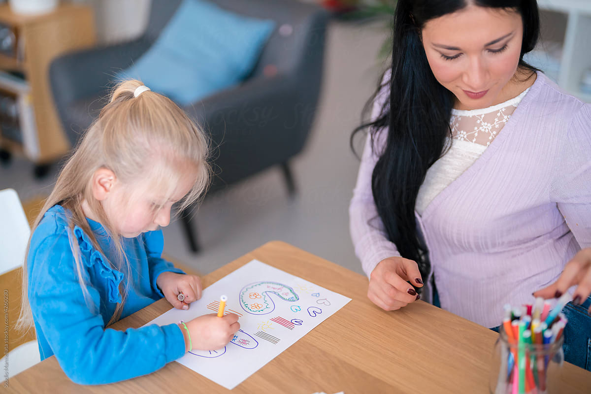 Woman helping girl to draw picture