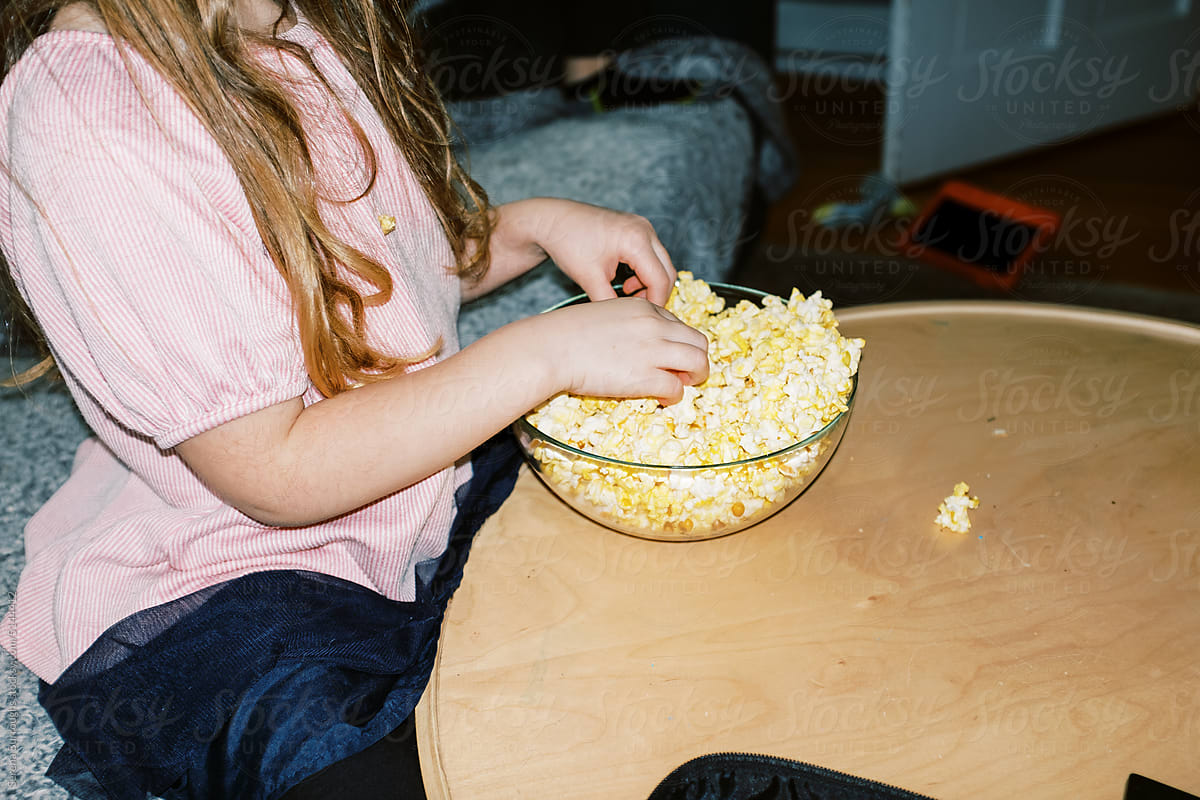 little girl eating popcorn at home in living room