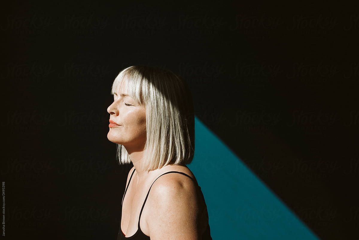 Portrait of blond woman in a sunbeam against a blue wall.