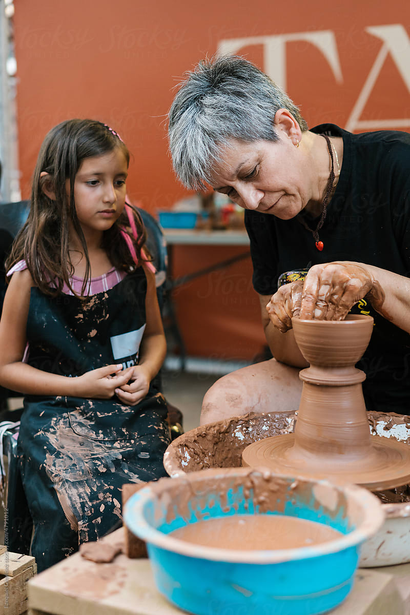 Woman shaping clay vase near girl