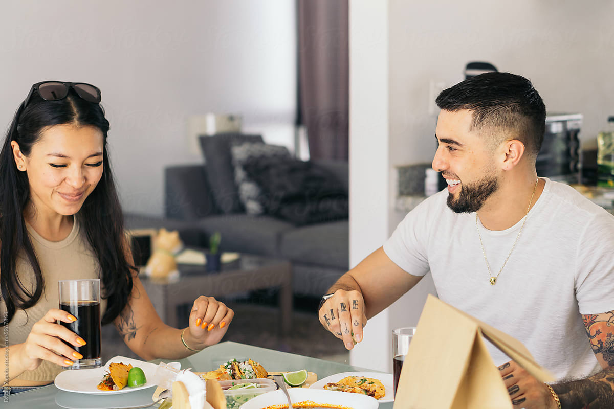 Couple at home laughing and eating tacos.