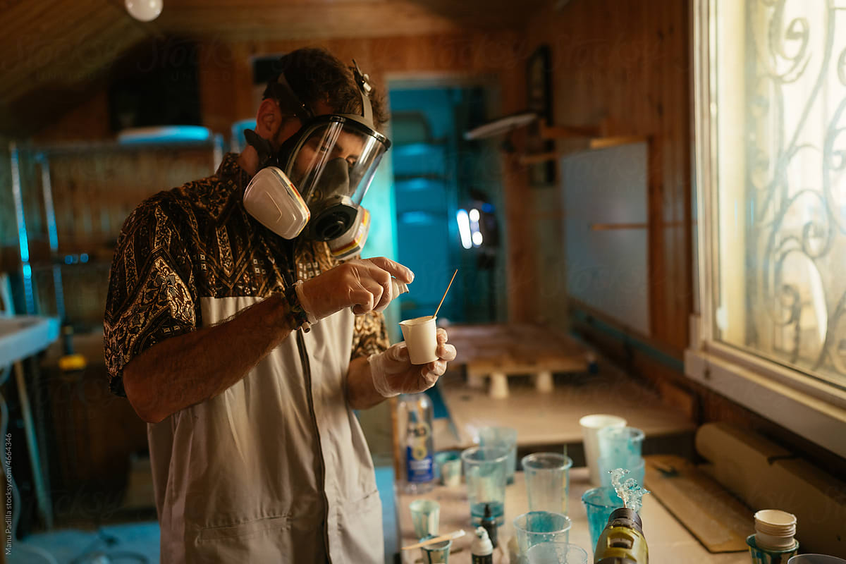 Serious man in respirator mixing resin in cup