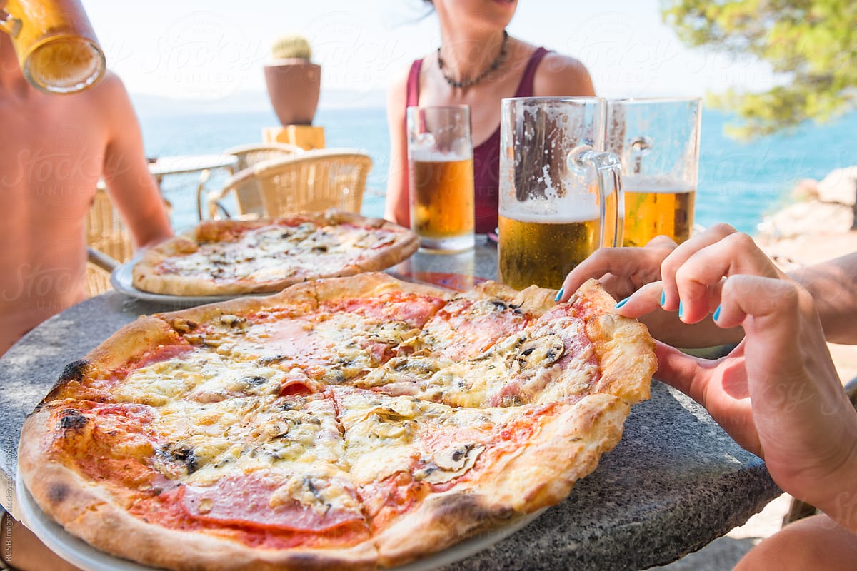 Group of friends having pizza and beer on a seaside terrace