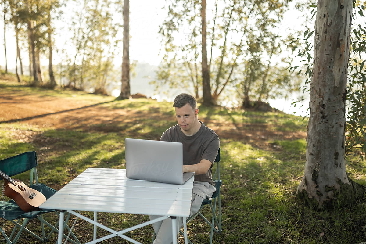 young man with down syndrome using a laptop in nature