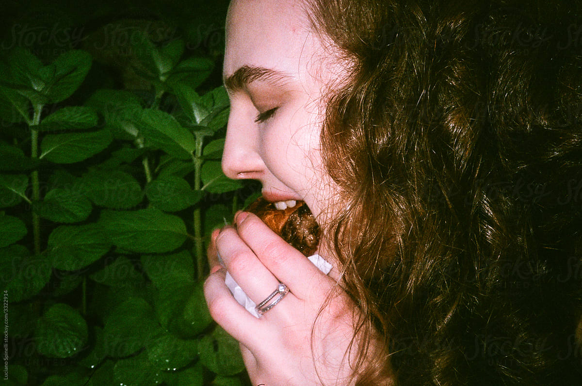 Woman eating a hamburger next to a green plant leaves