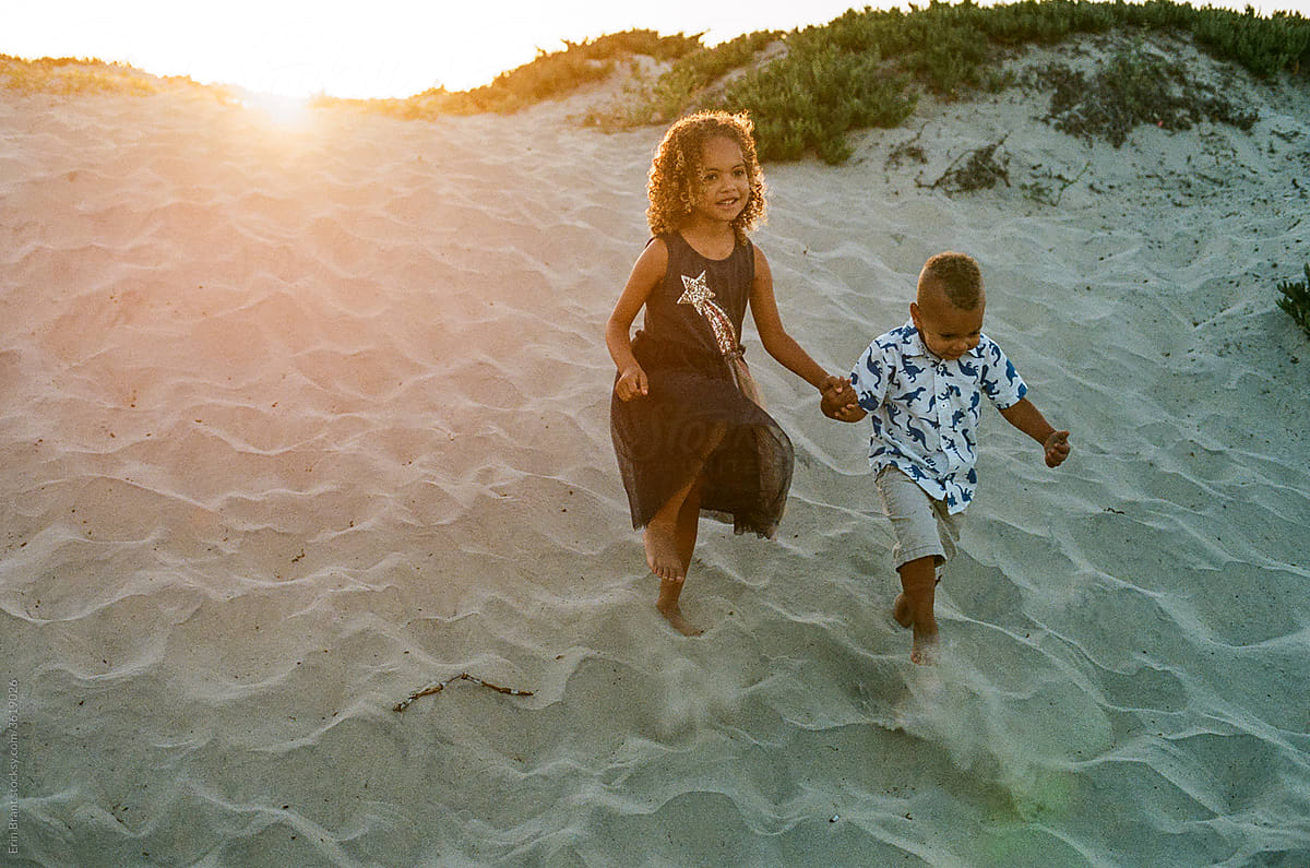 Mixed race siblings walking in sand at sunset