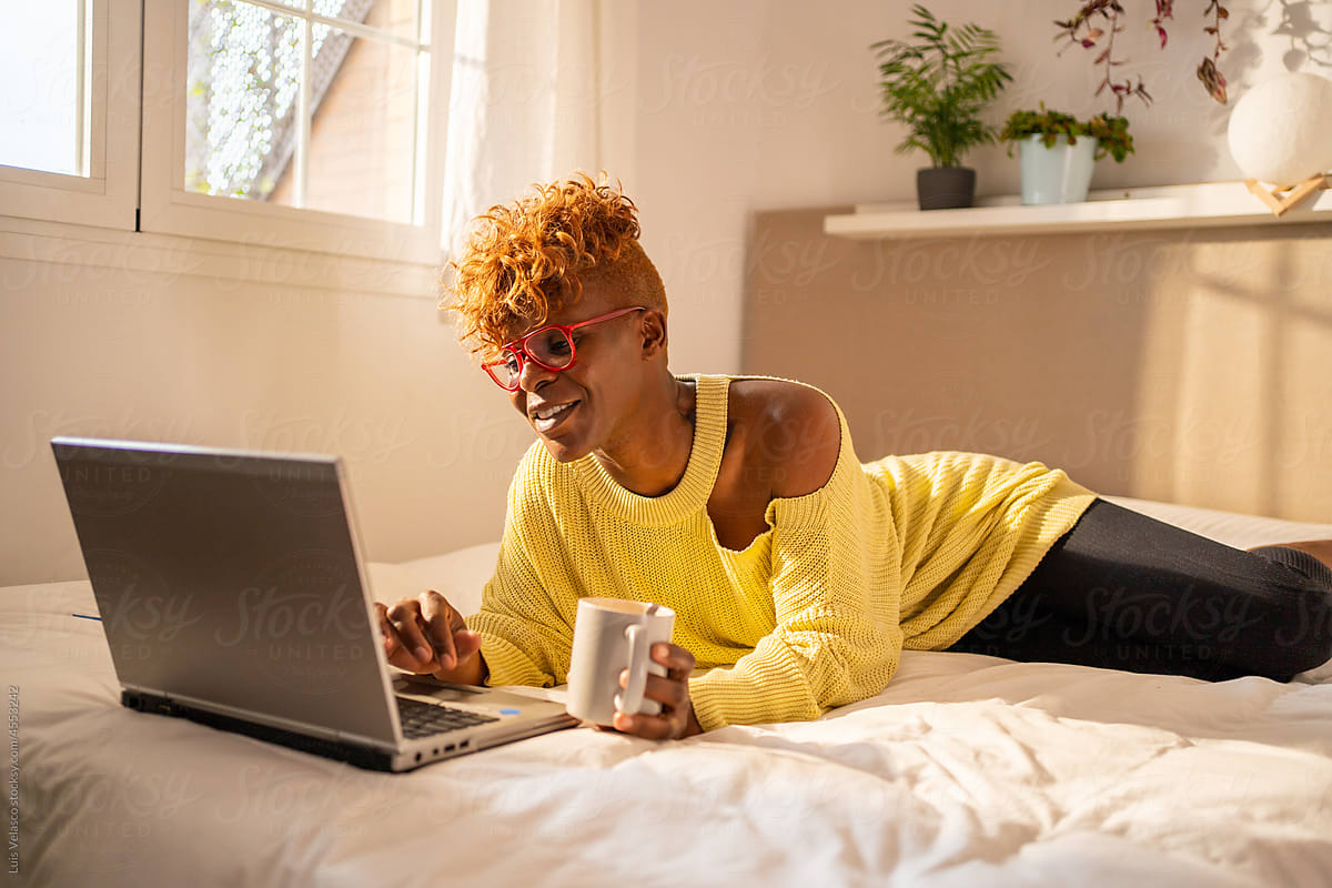 Black Woman With Laptop Having A Coffee Laying On The Bed.
