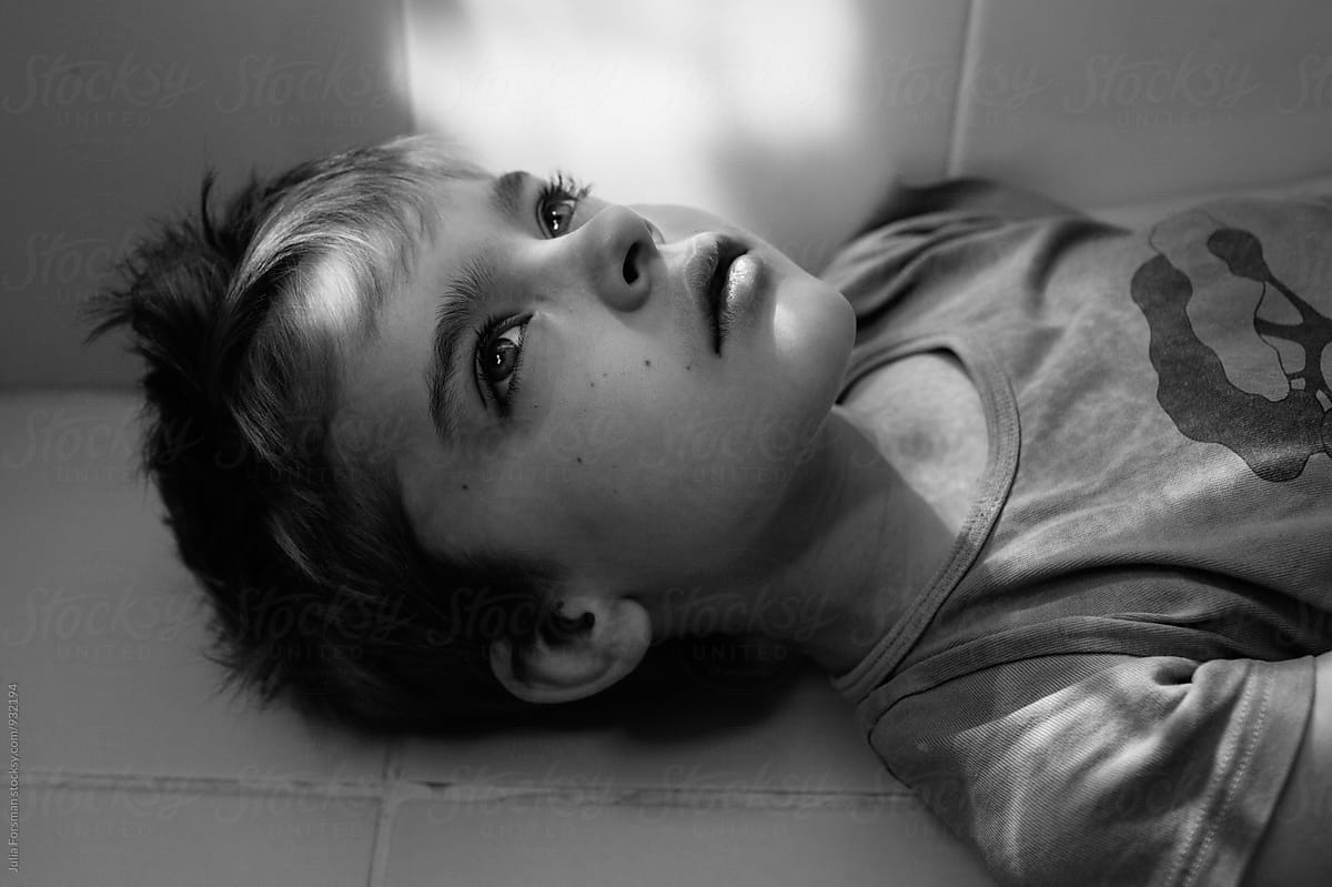 Black and white close up of thoughtful boy laying on bathroom floor.