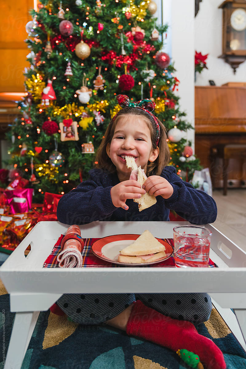 Child Biting a Sandwich under the Christmas Tree