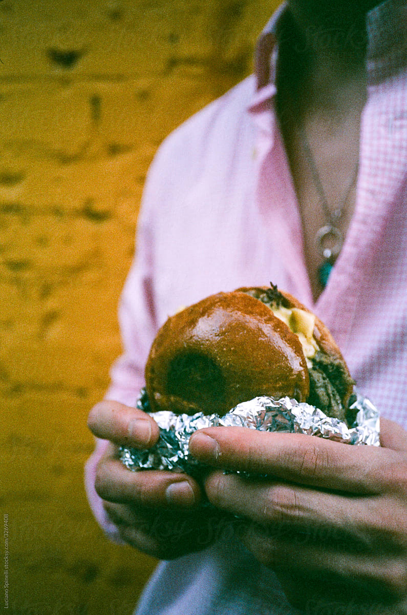 Anonymous man in a pink shirt with a burger in his hands