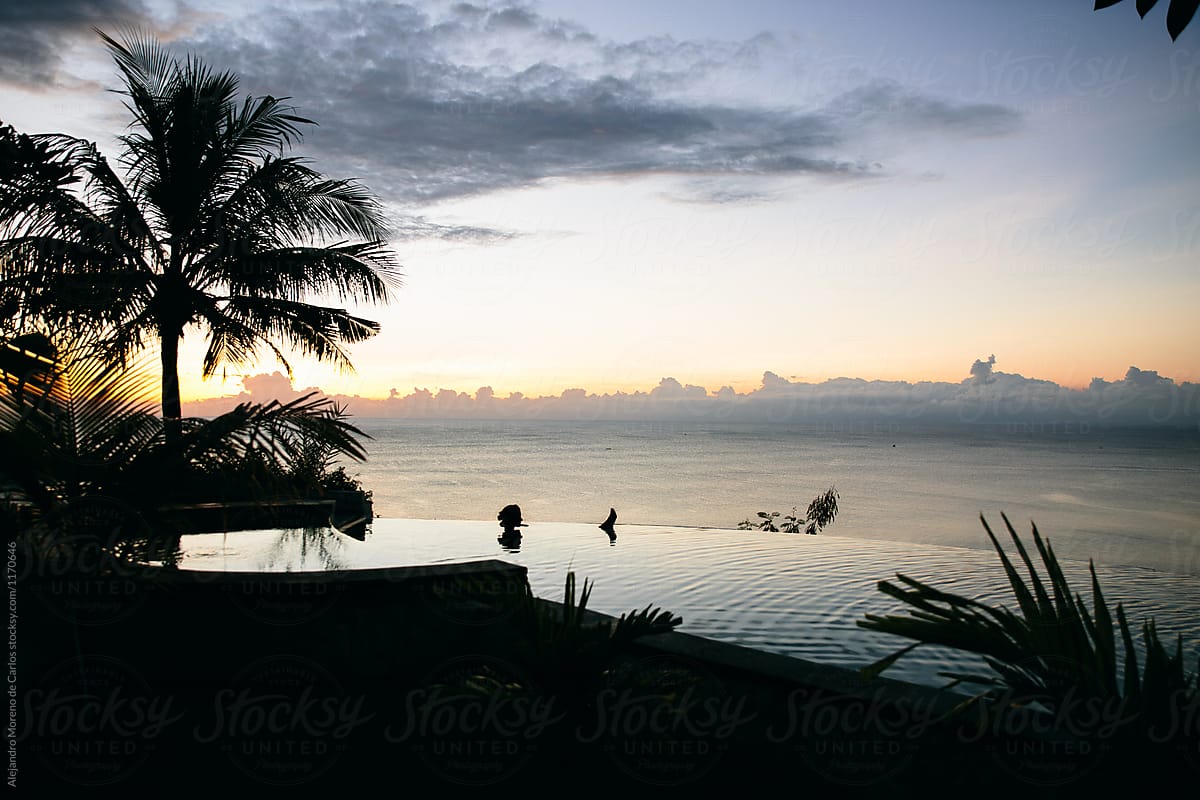 Young woman relaxing at an infinity pool at sunset on a tropical
