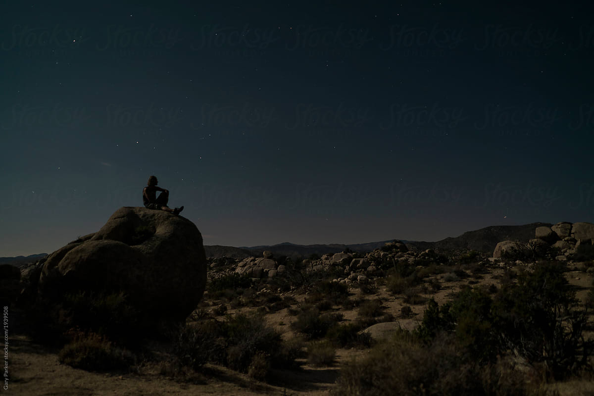 A young man sitting under the night sky in Joshua Tree National Park