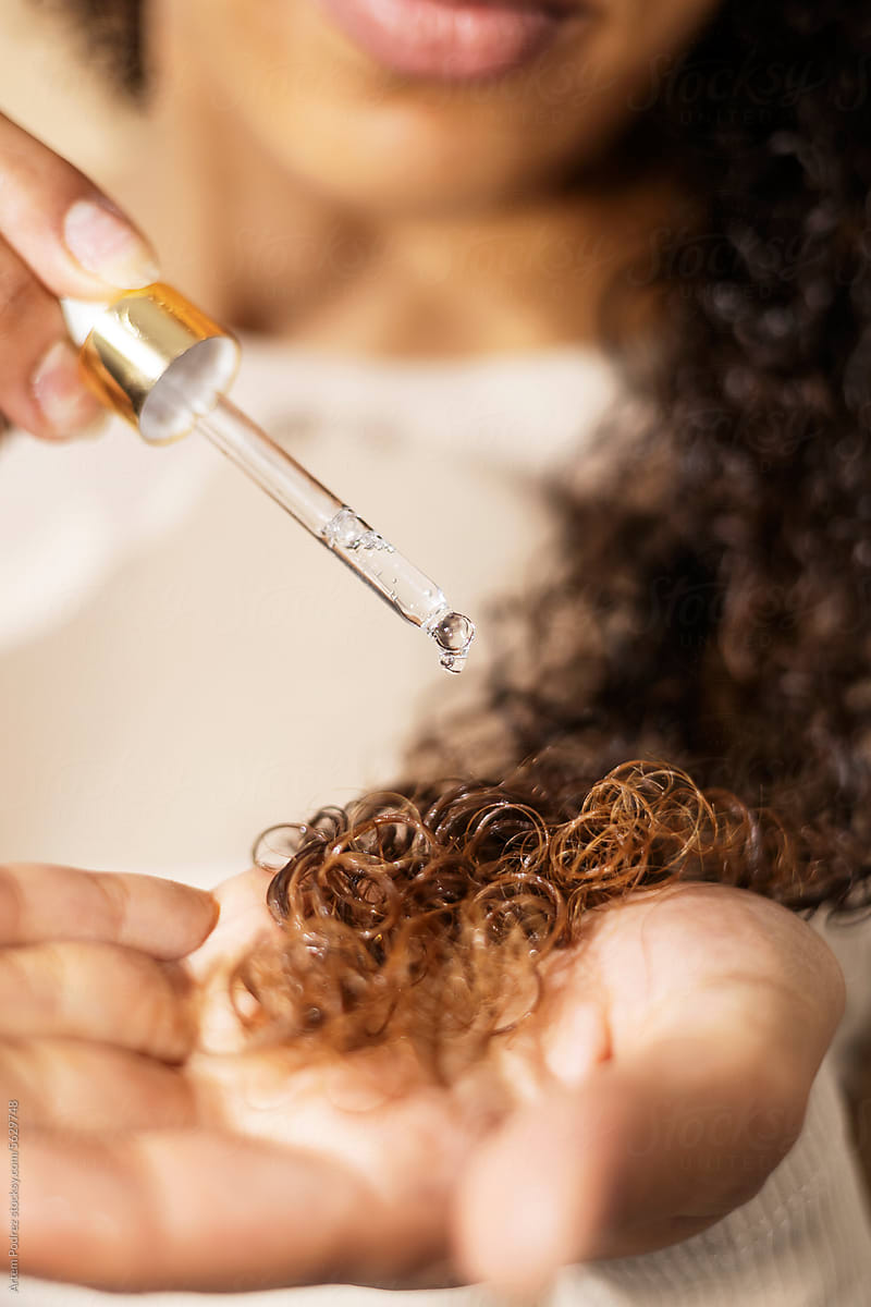 a woman takes care of her curly hair with hair oil