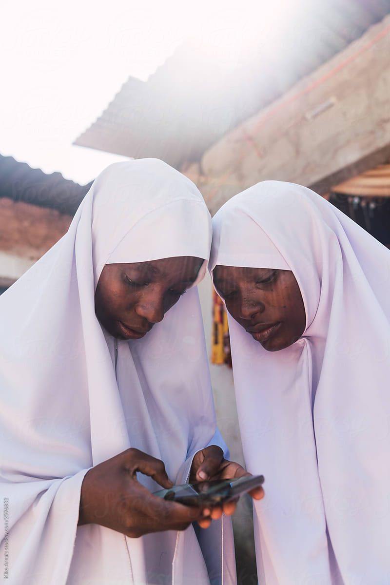 Two young woman dressed with muslim school uniforms, searching information on the phone