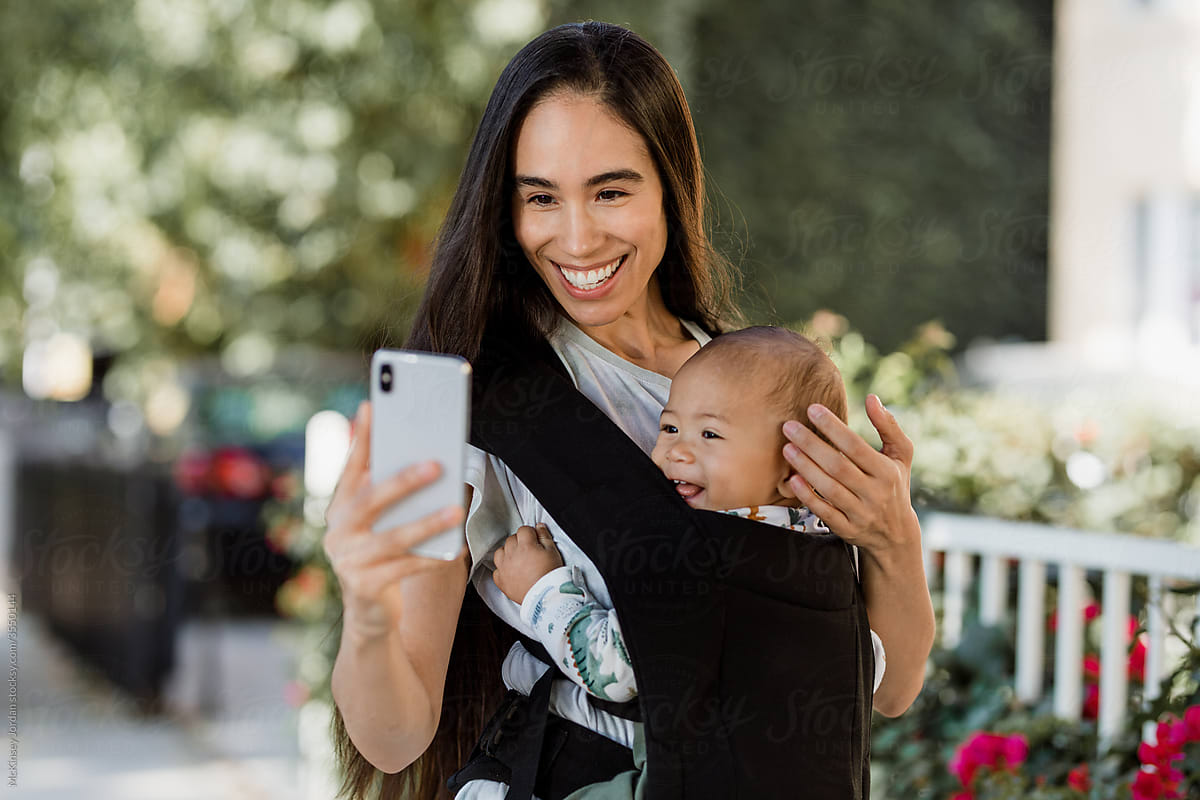 Woman Uses Smartphone While Carrying Baby