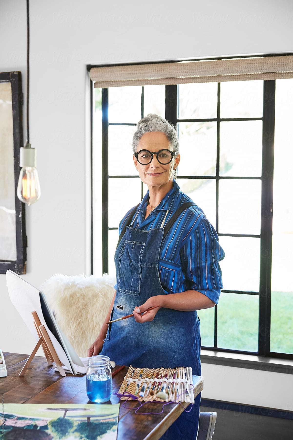 Artist portrait of mature woman with grey hair in her art studio in California