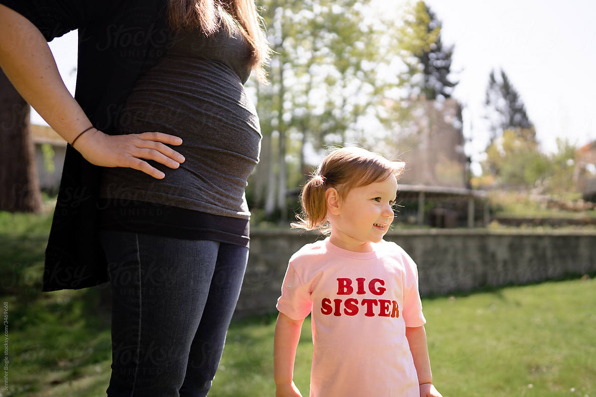 Profile of cute toddler in big sister shirt and her pregnant mom