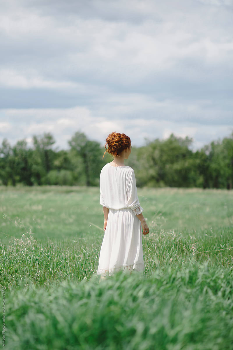 Beautiful young redhead  woman standing in a field in a white dress