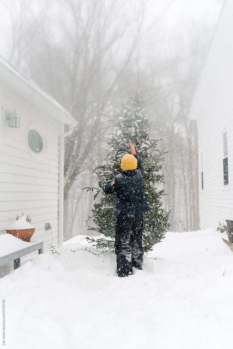 boy putting lights on outside Christmas tree on a snowy day