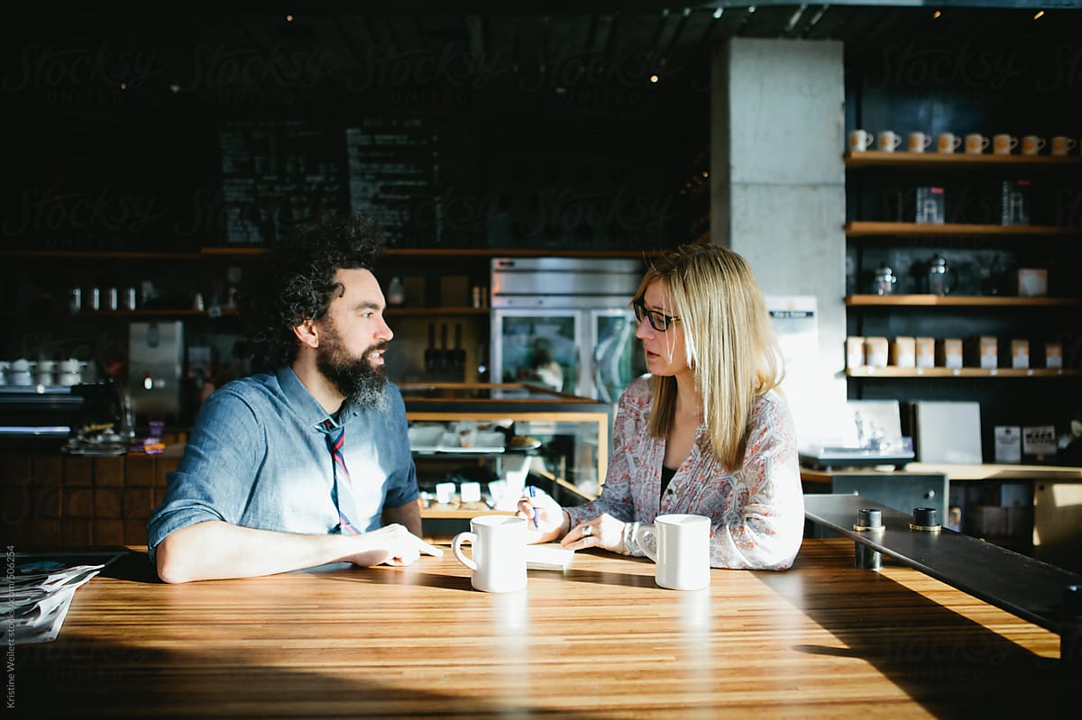Man And Woman Having A Conversation Over Coffee In A Cafe By Stocksy