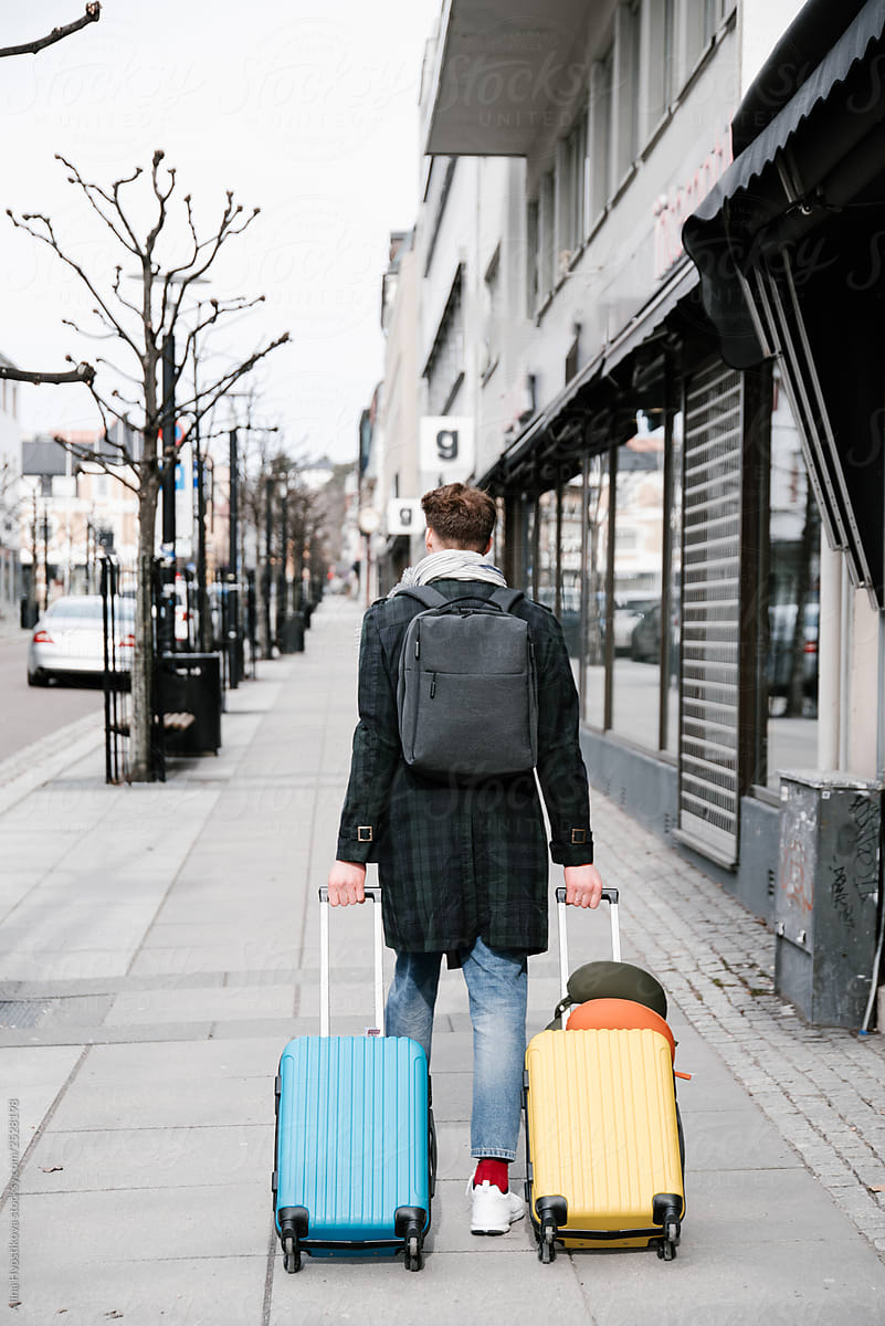 Young male with colourful suitcases walking on street