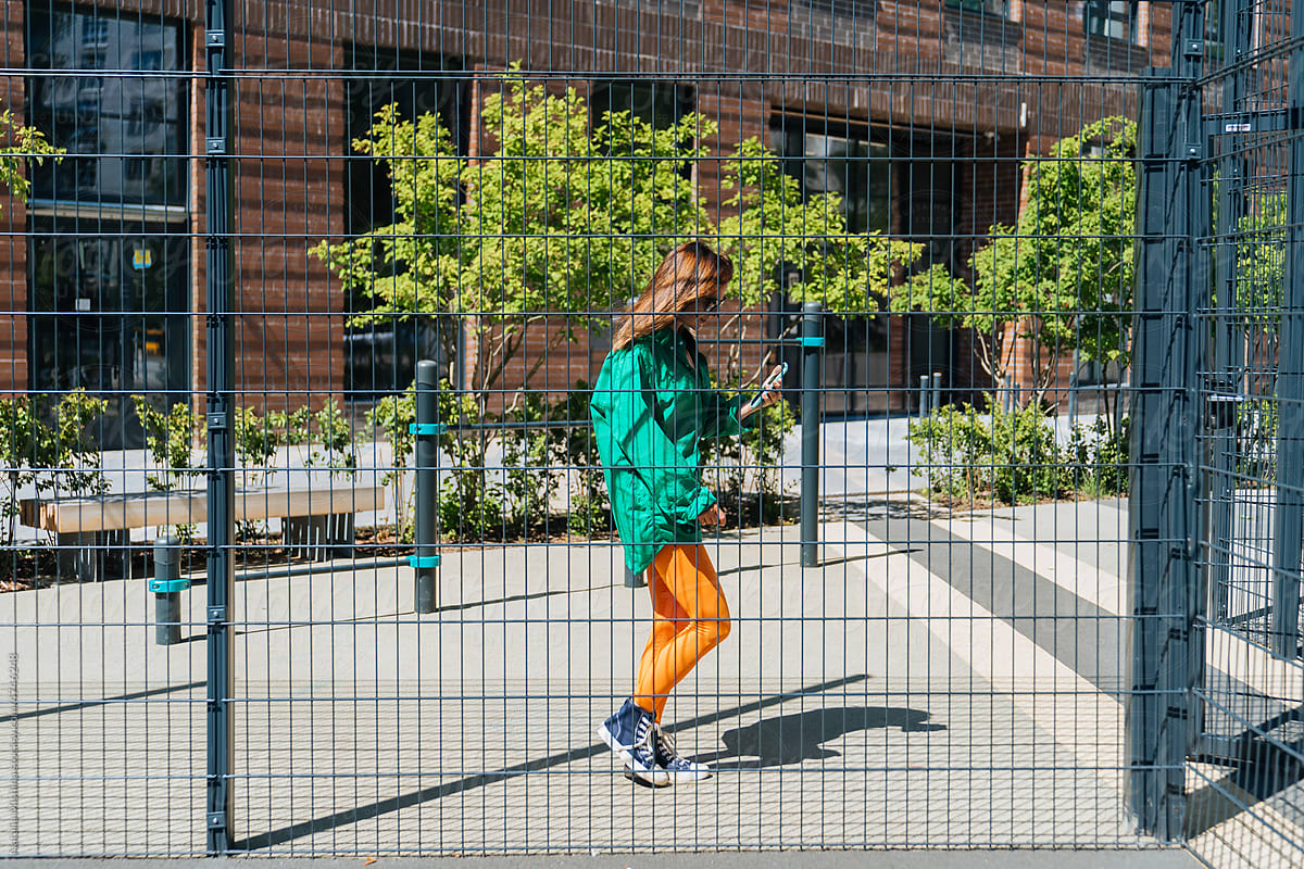 A girl in bright clothes behind the fence of the playground.