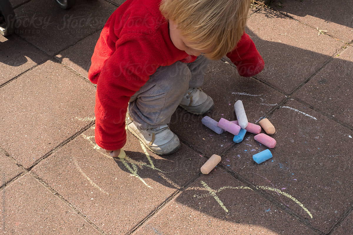 A child is drawing by chalk on a pavement
