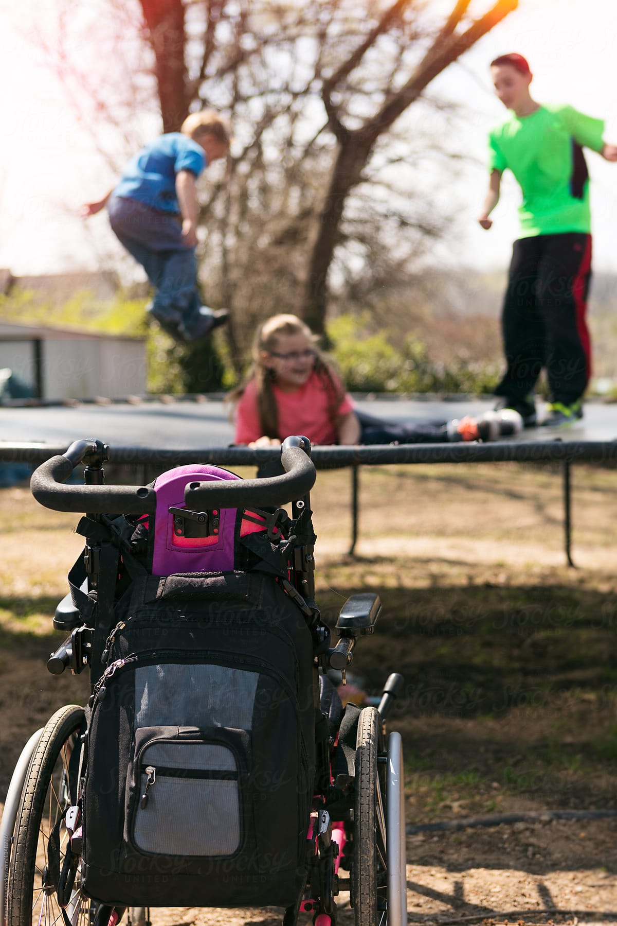 Wheelchair In Foreground As Girl Bounces With Friends