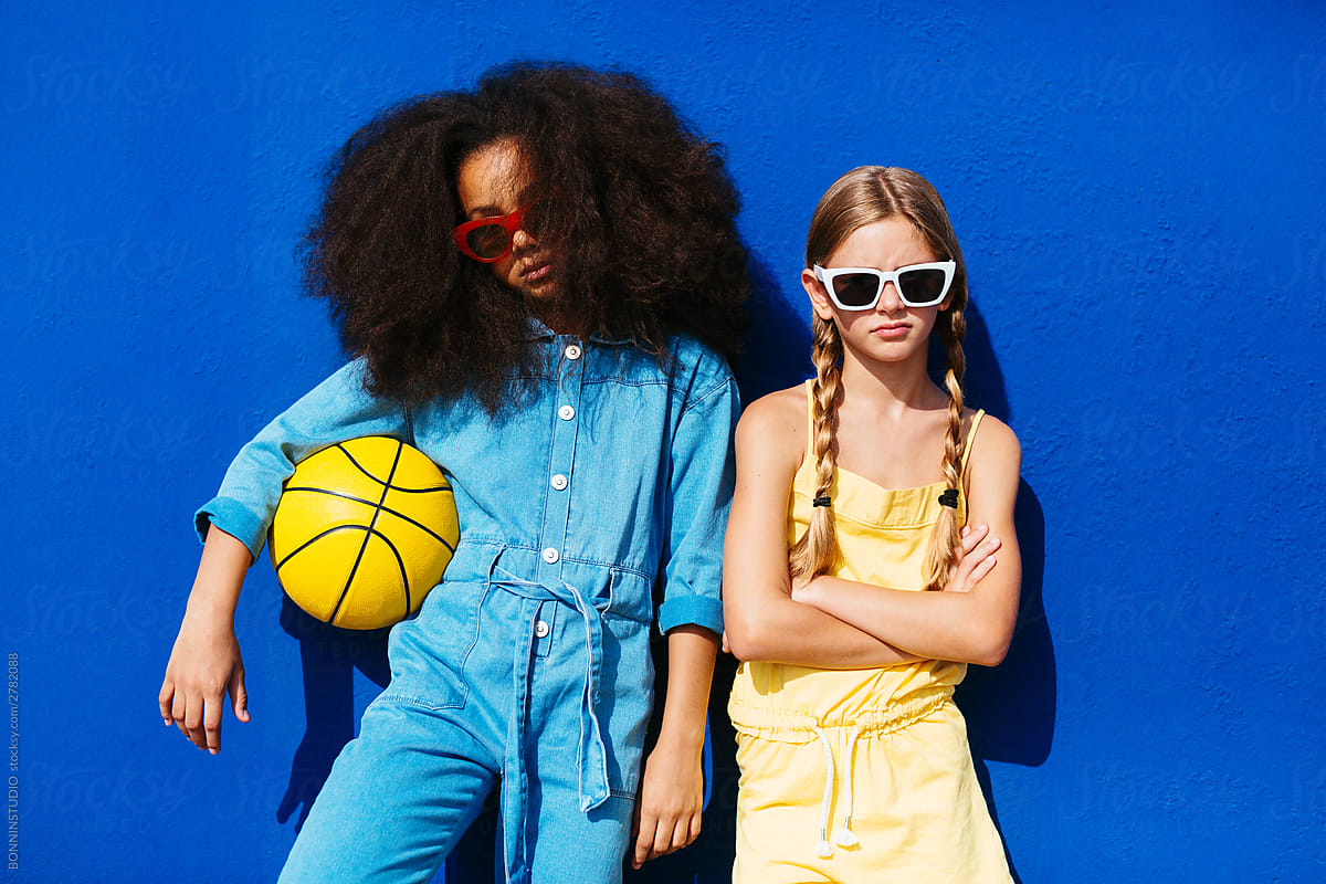 Smug multiethnic friends in trendy sunglasses holding ball while standing on street
